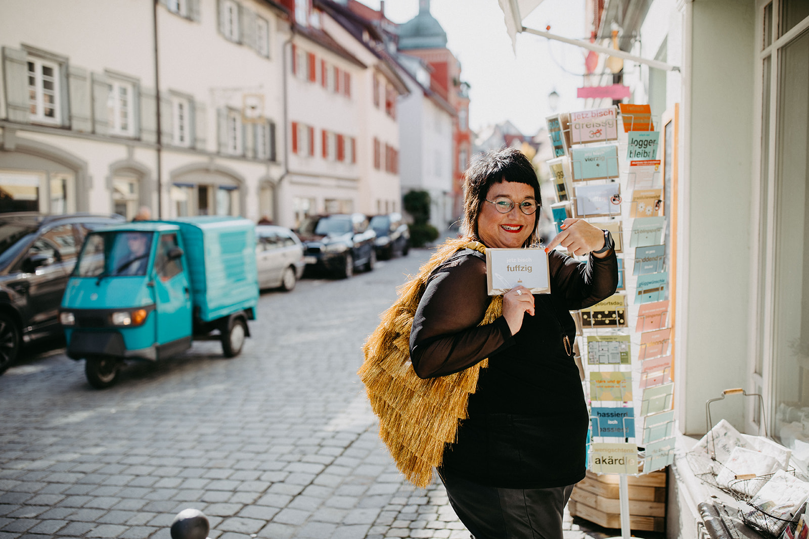 Sabine, die Speakerin für Frauen ist und Vorträge für Frauen hält, steht vor eine Geschäft und zeigt auf eine Karte mit dem Titel fünfzig. 